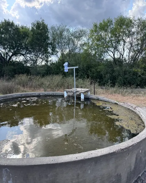 A Trivertix monitor on a T-shaped pole over a round concrete stock tank, with trees behind