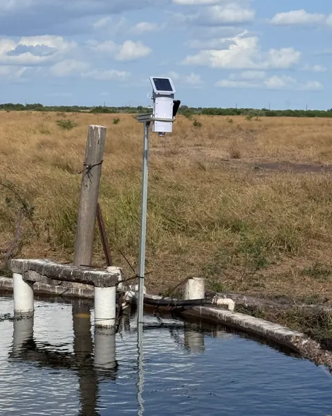 A Trivertix monitor on a tall pole beside a concrete stock tank in open pasture